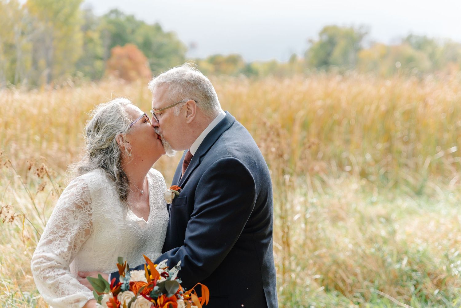 Intimate wedding moment captured in golden field during fall season.