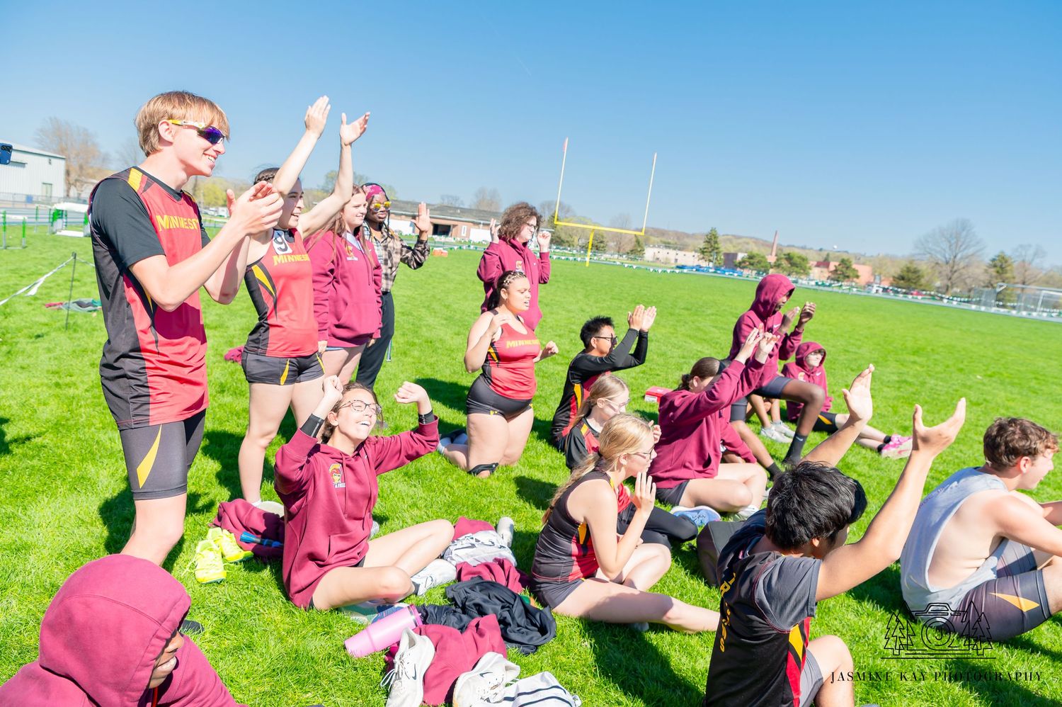 Sports team sitting on grass field during practice while coach gives instructions.