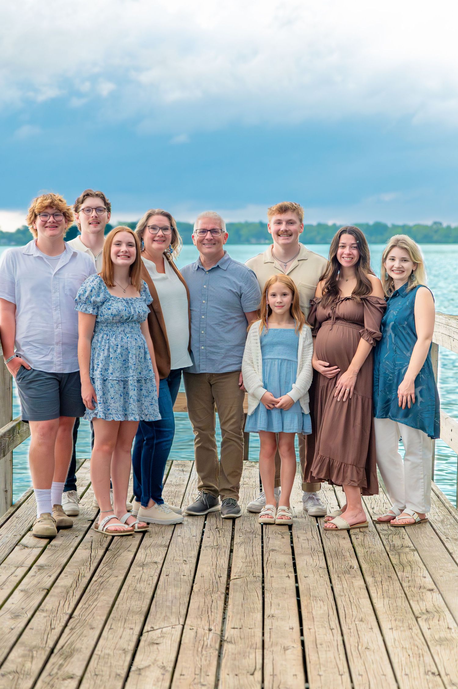 A group poses together on a wooden dock overlooking a tropical beach with blue water and sky in the background.