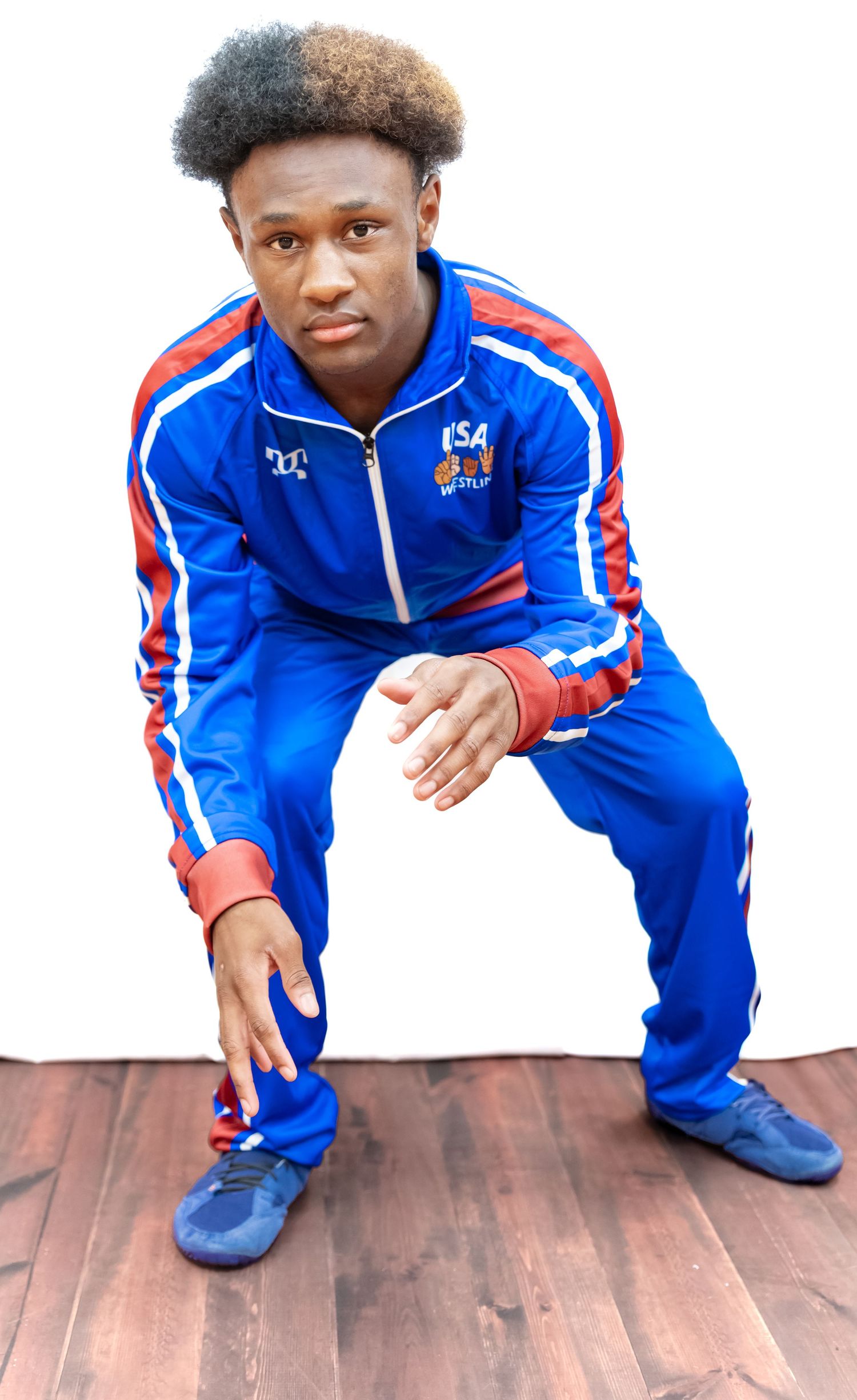 Person in blue USA team tracksuit crouches on hardwood floor in athletic pose.