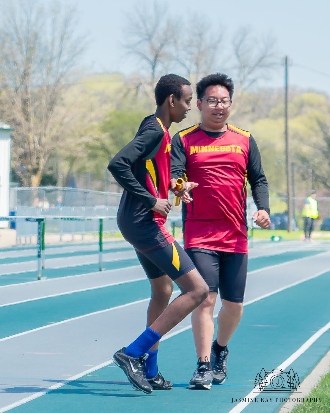 Two athletes practicing track sprinting form and technique on an outdoor running track on a sunny day.
