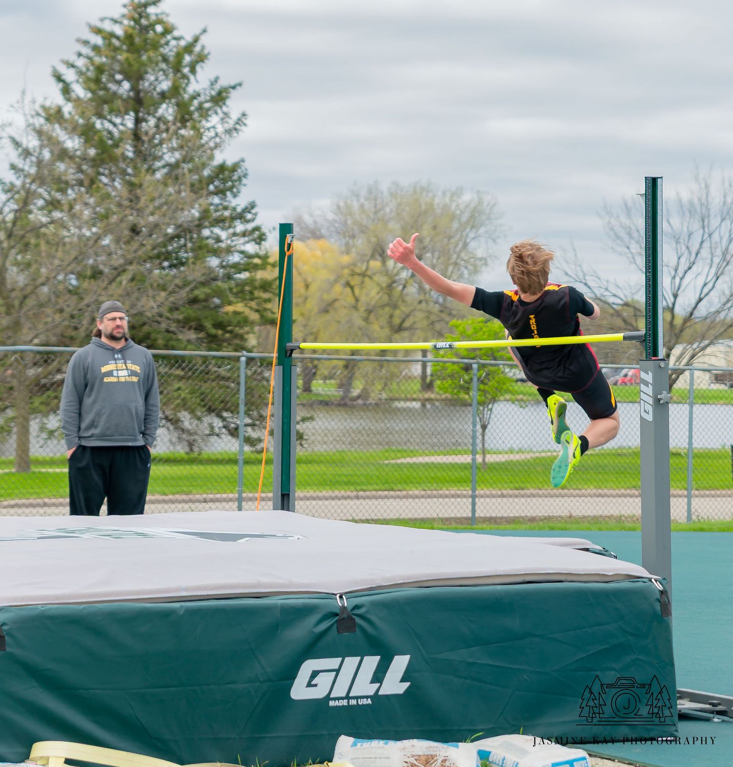 Athletes practicing track and field exercises on an outdoor court with bleachers visible in the background.
