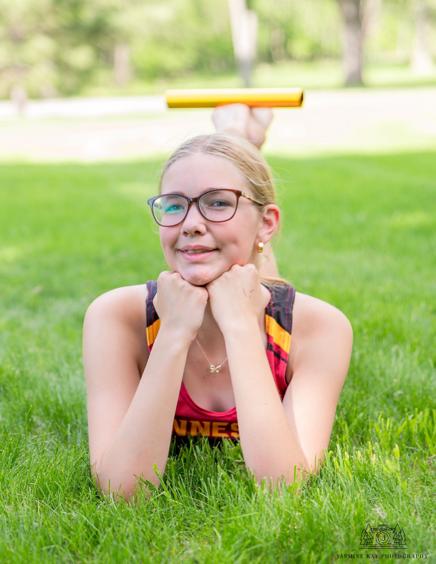 A person wearing glasses lies on green grass in a sunny outdoor setting.