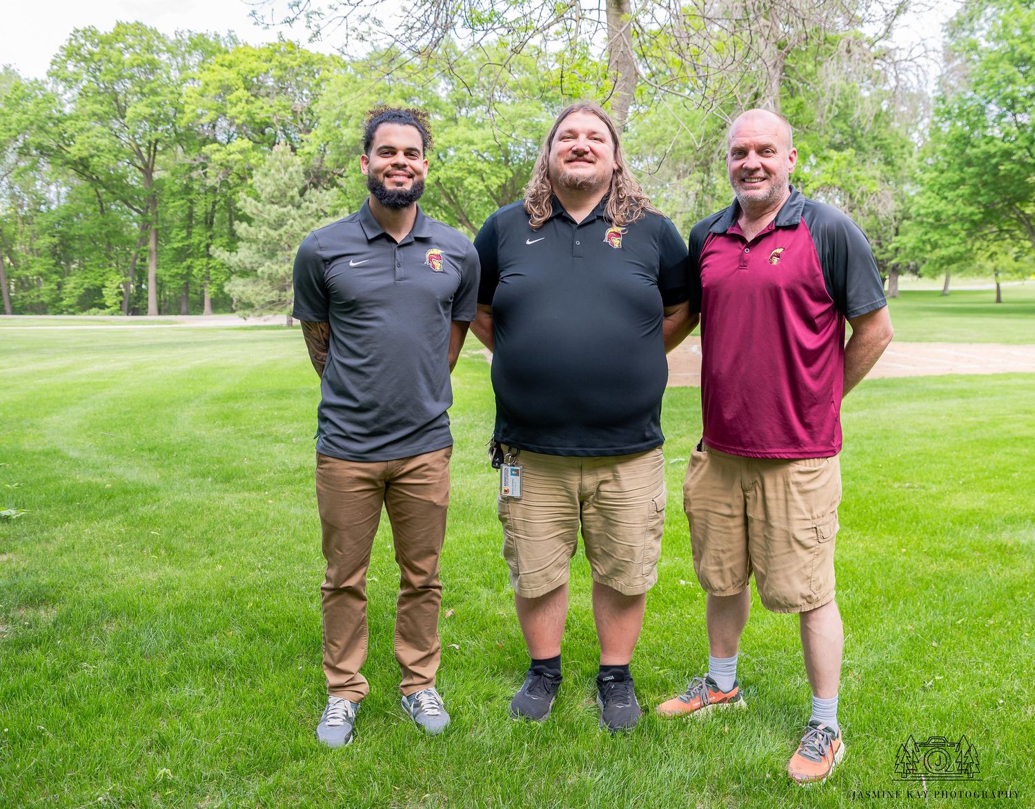 Three people stand together on a lush green golf course wearing casual polo shirts and shorts.