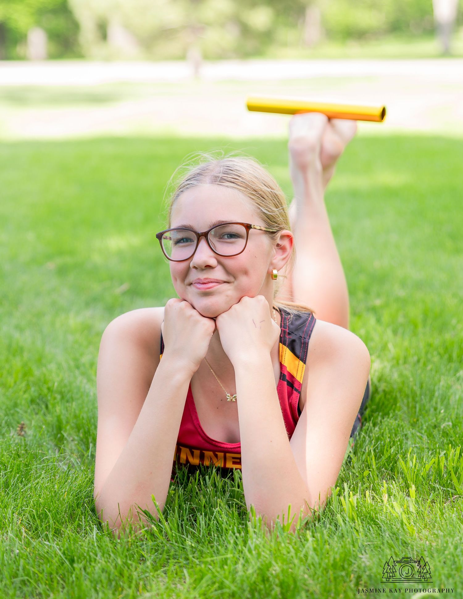 A person wearing glasses lies on green grass while smiling and relaxing outdoors on a sunny day.