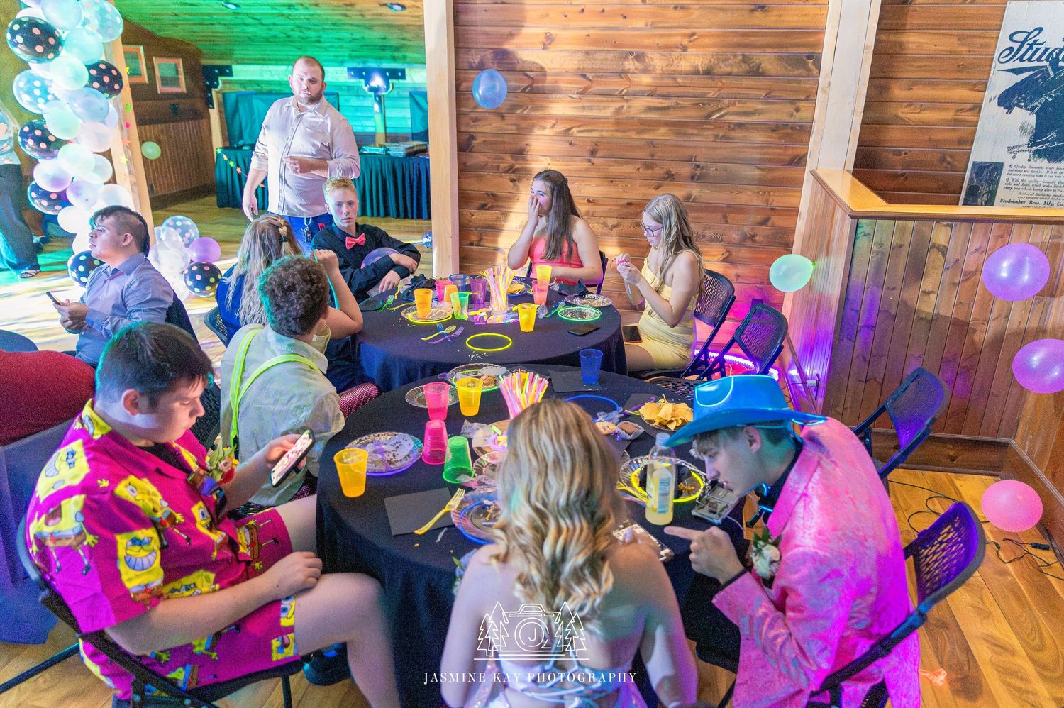 A group enjoys a lively celebration with colorful lighting in a rustic wood-paneled venue.