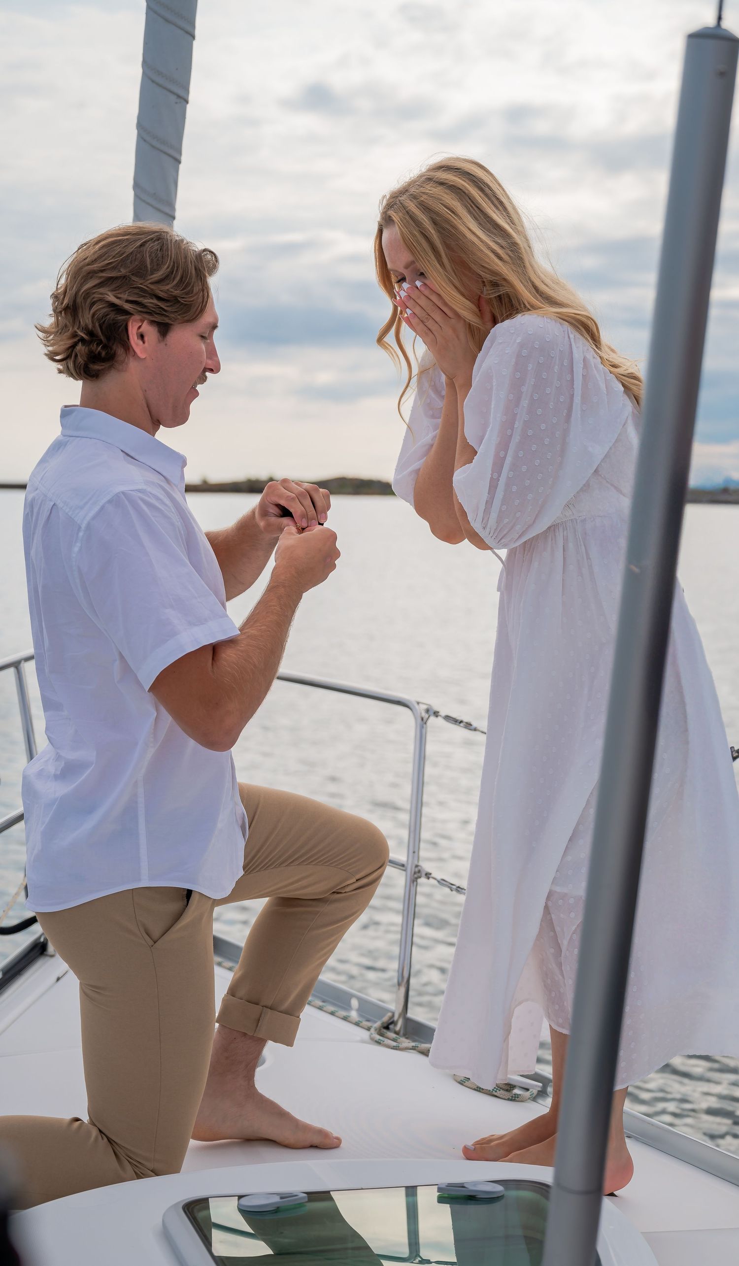 Surprise proposal moment captured on a boat with water and cloudy sky backdrop.