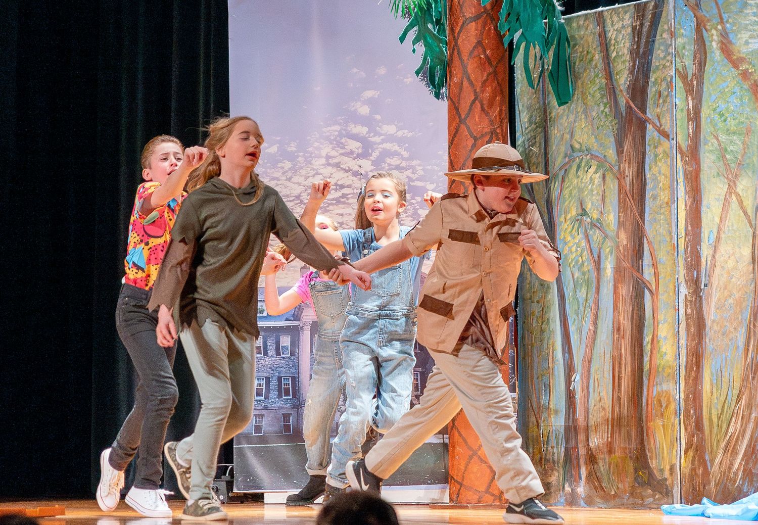 Performers on stage with painted forest backdrop during a theatrical production.