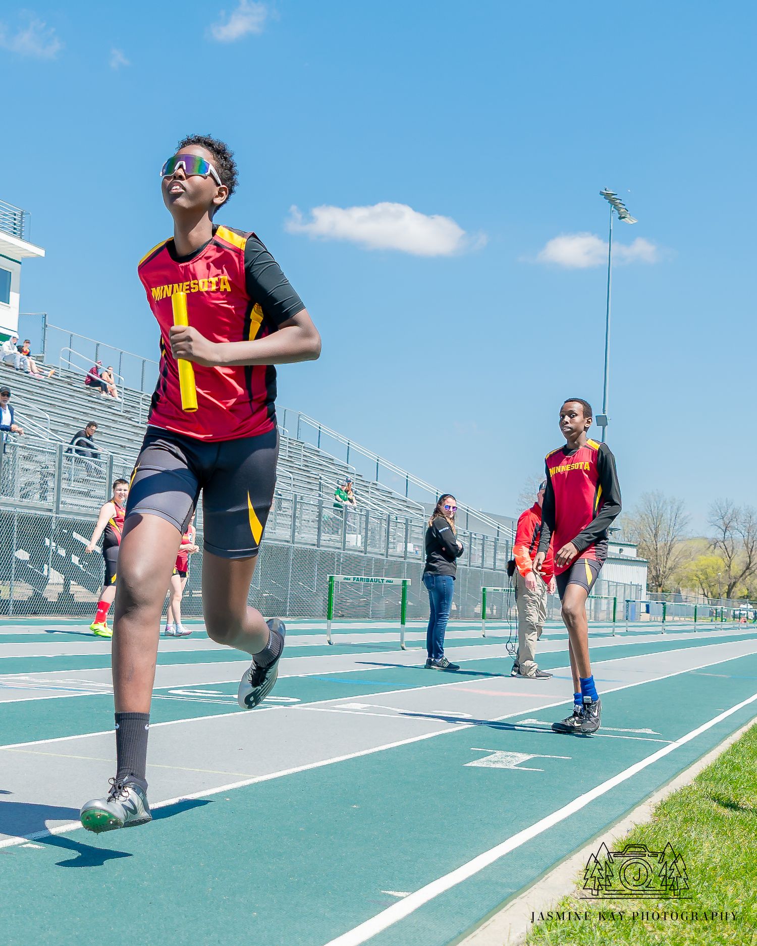 Athletes practicing sprint technique drills on outdoor track with blue surface.