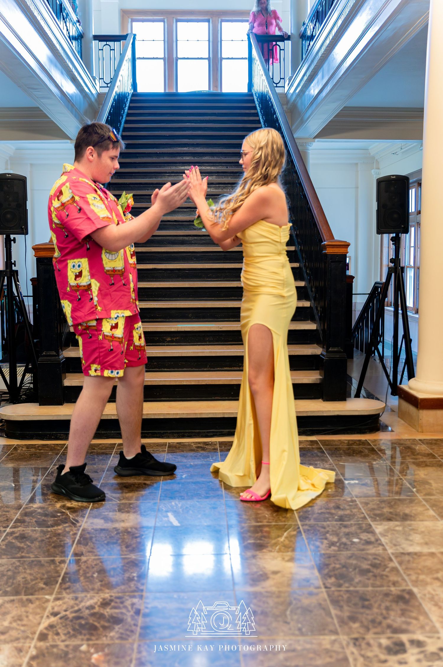 A couple dancing together on a marble floor in front of stairs, with the person in yellow leading their partner.