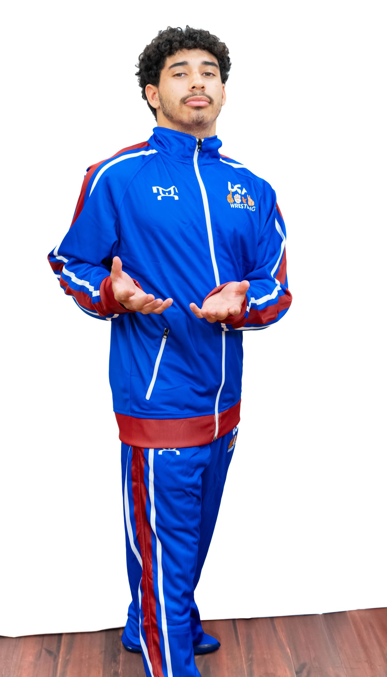 Athletic person wearing blue and red USA team tracksuit stands with open gesture on wooden floor.