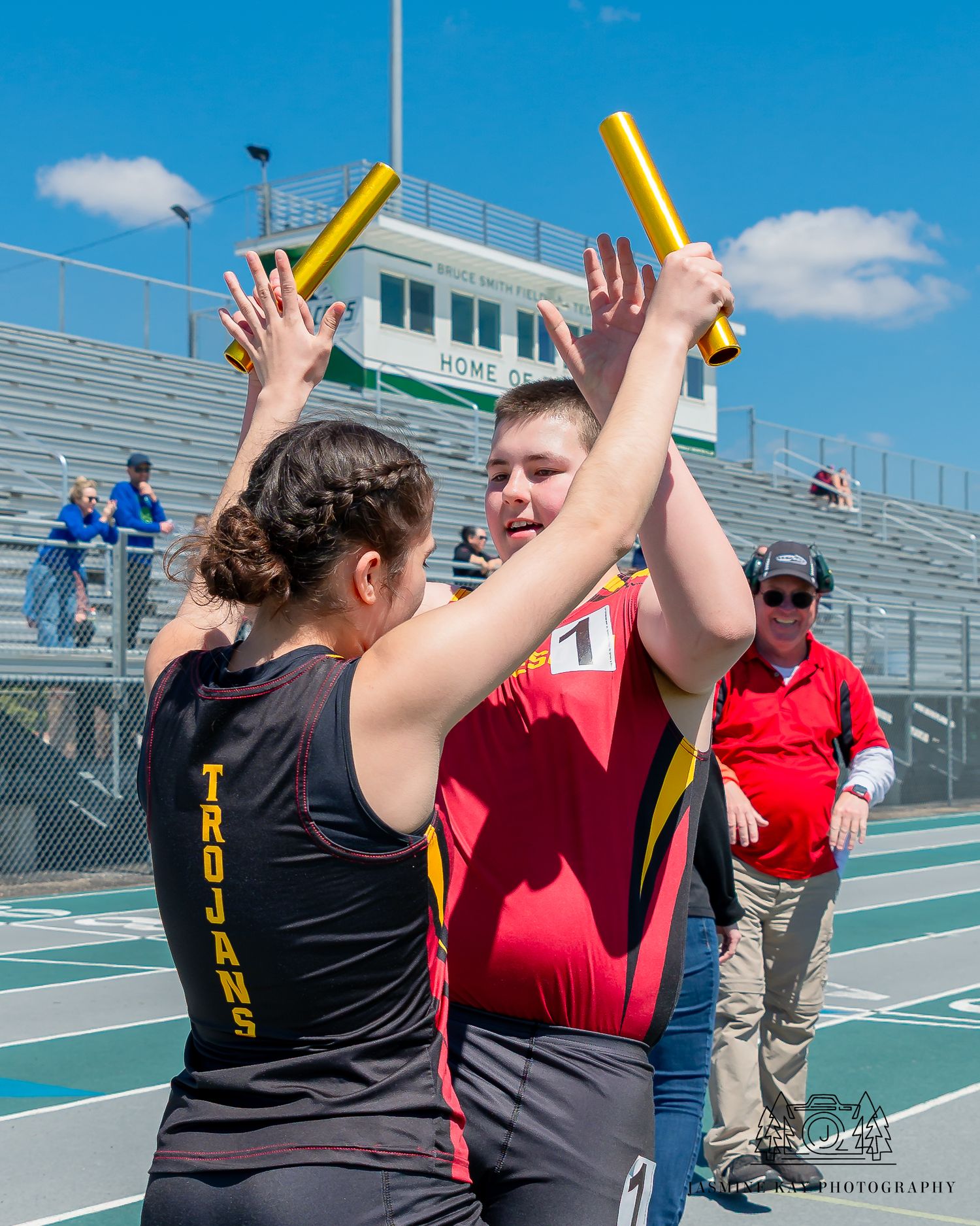 Two people celebrate with raised arms and high-fives on an outdoor tennis court on a sunny day.