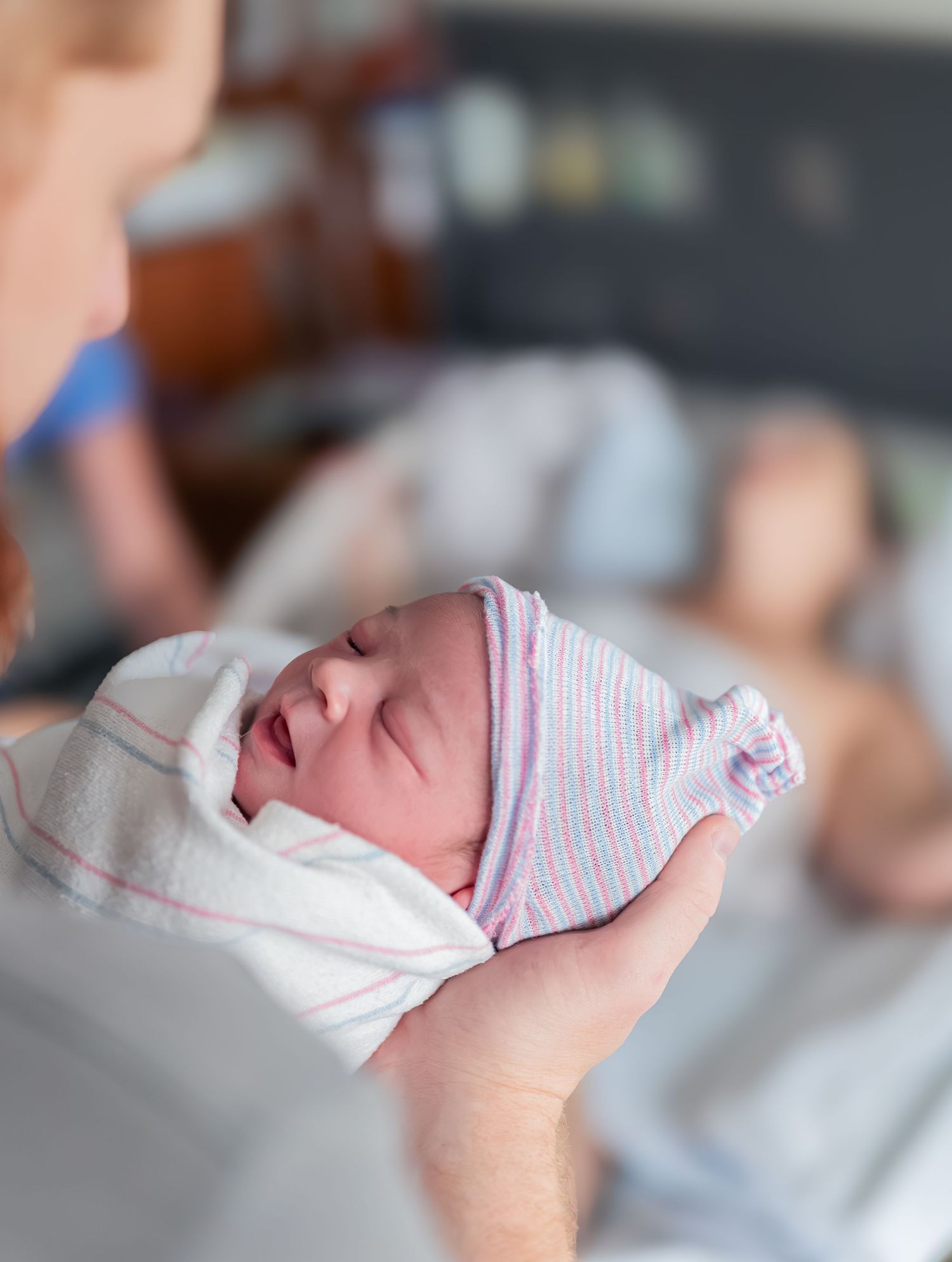 A sleeping newborn baby wearing a white and pink striped onesie rests peacefully in soft lighting.