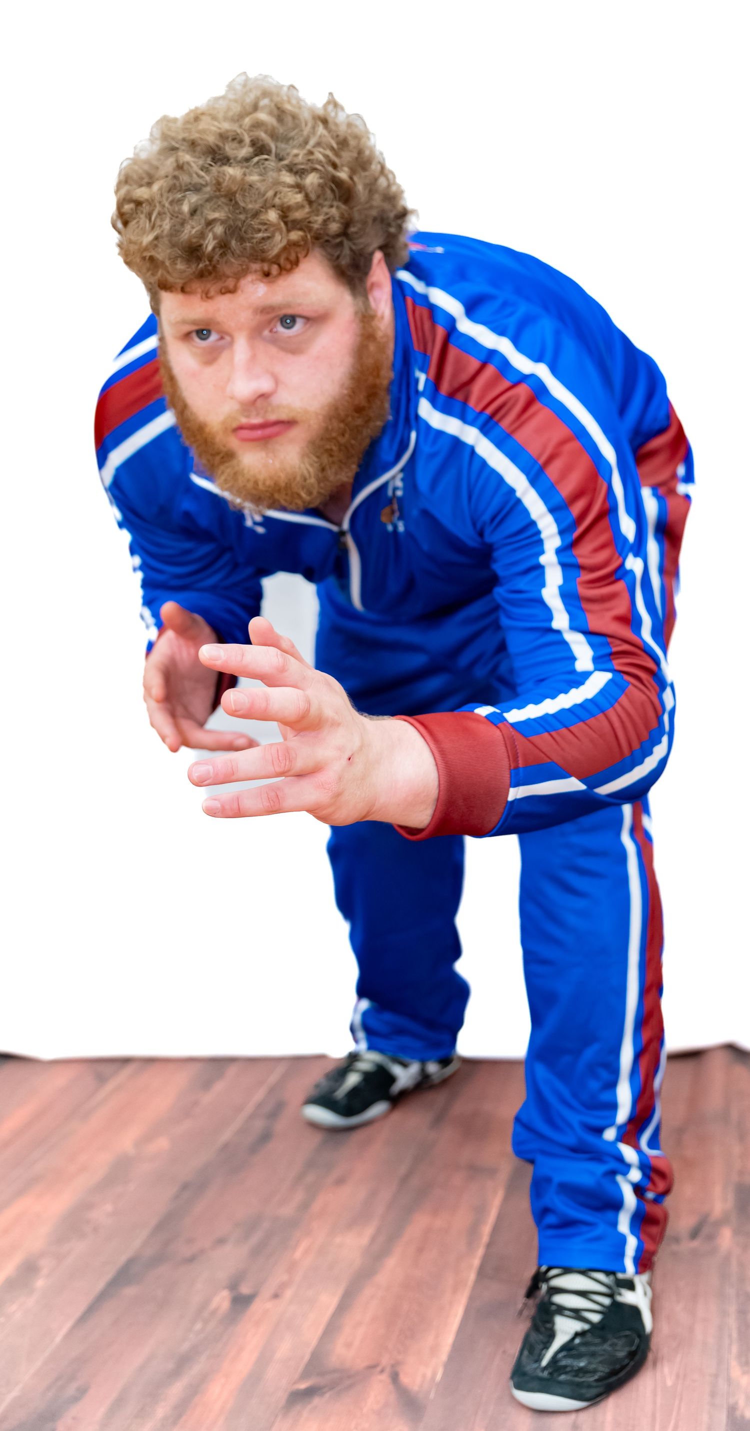 Person in blue and red tracksuit demonstrating crouching movement sequence on wooden floor.