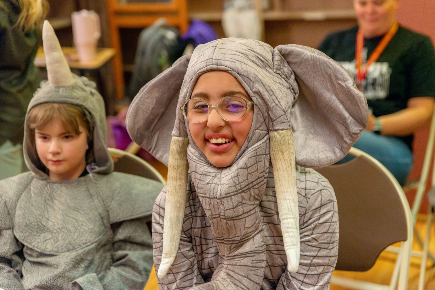 Students sitting in a classroom wearing winter accessories and smiling.