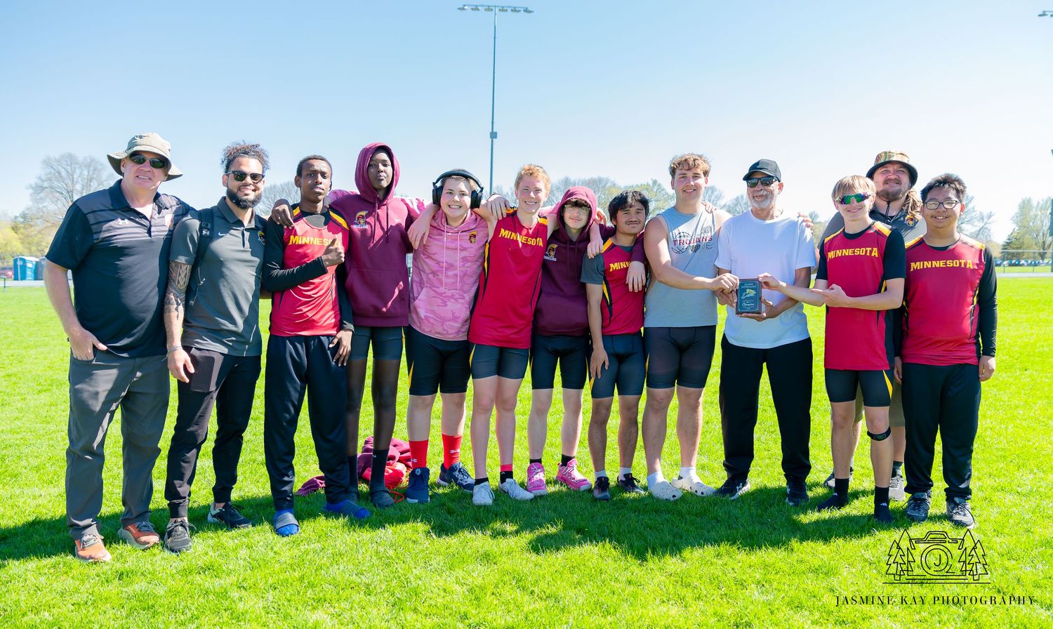 A group of people wearing pink and black uniforms stand together outdoors on a sunny day.