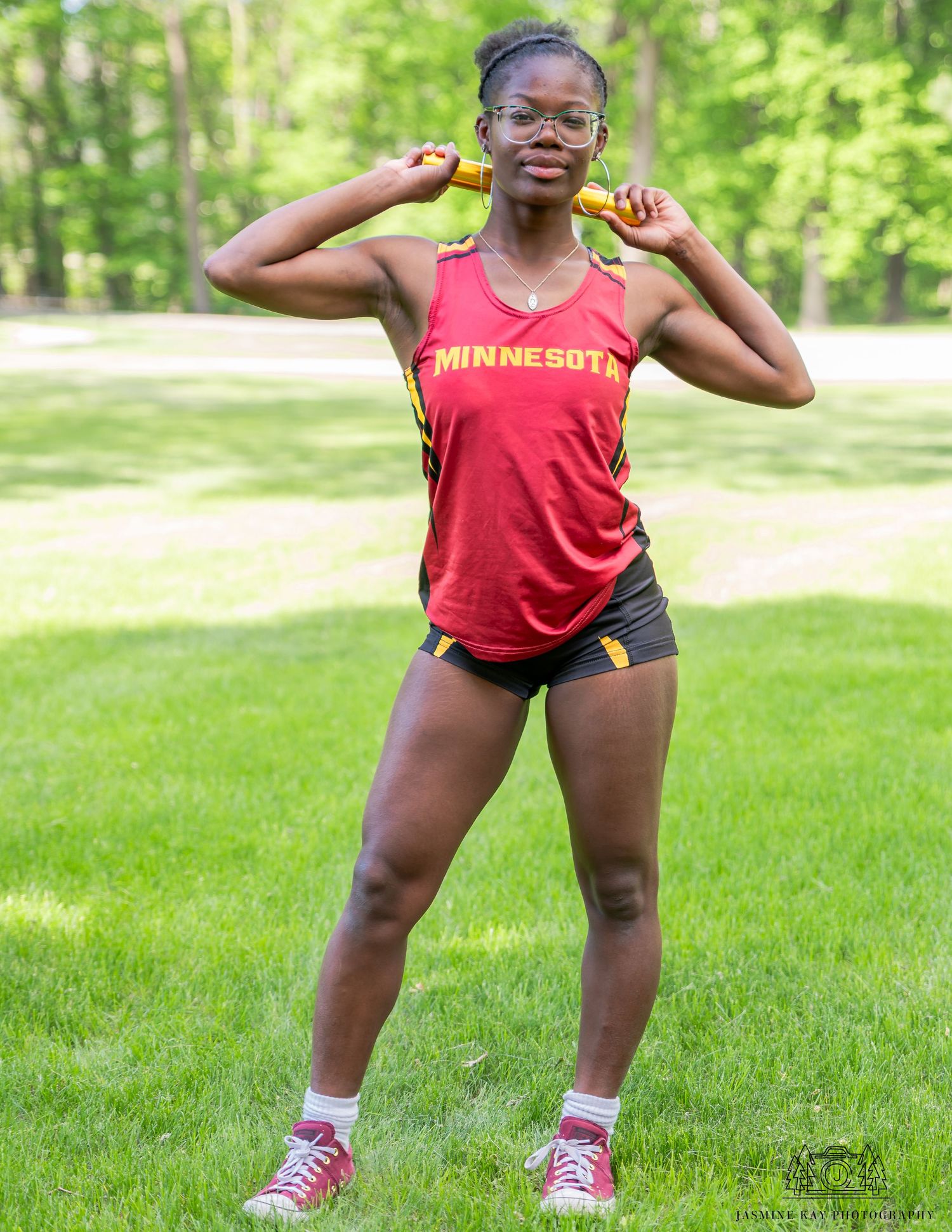 Athlete in red tank top and shorts stretches and warms up on green grass field.