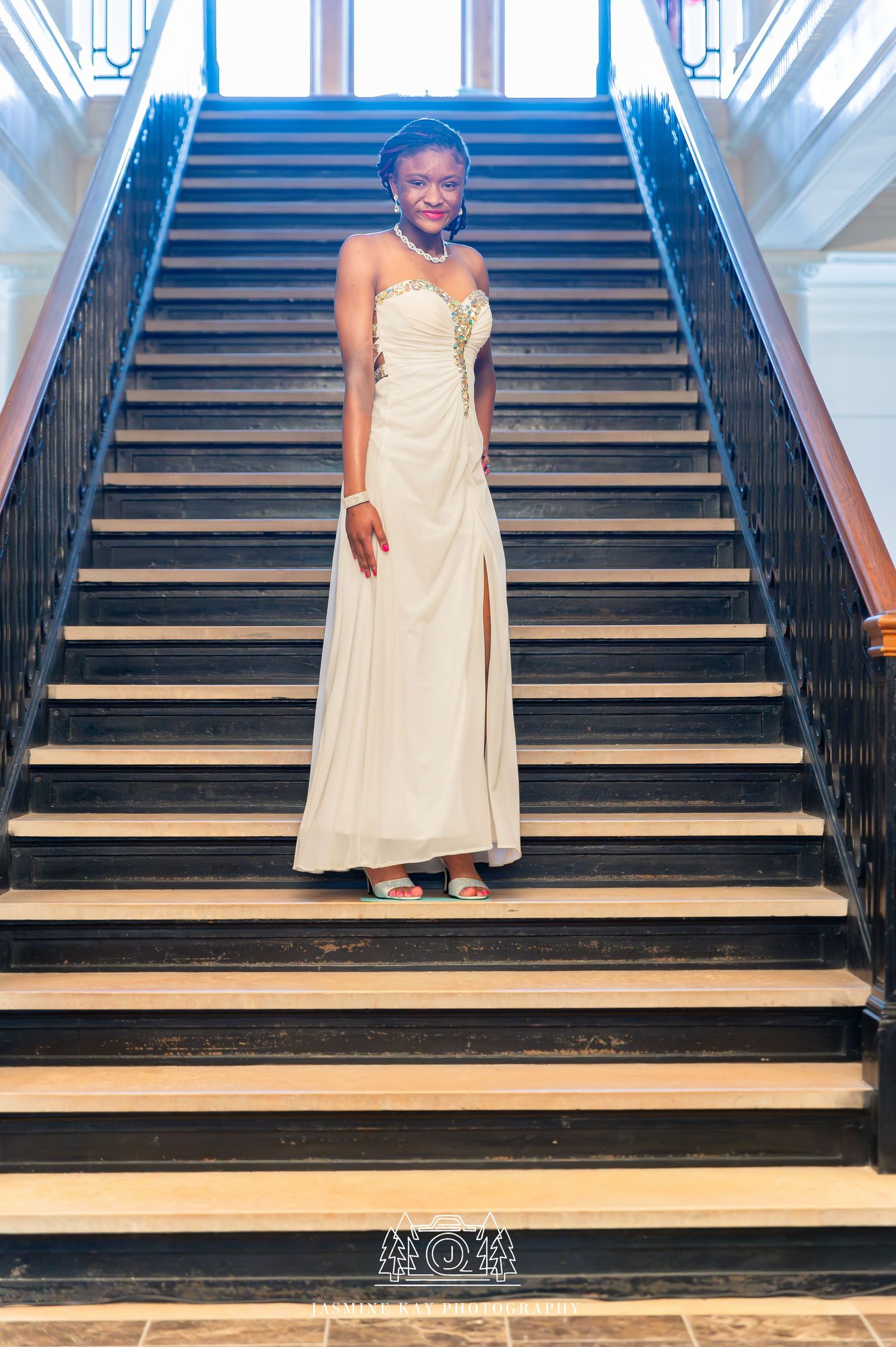 A person stands gracefully on wooden stairs while wearing a light-colored formal dress.
