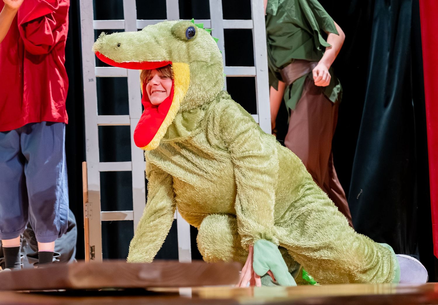 A person in a bright yellow dinosaur costume performs on a wooden stage with others in colorful outfits.
