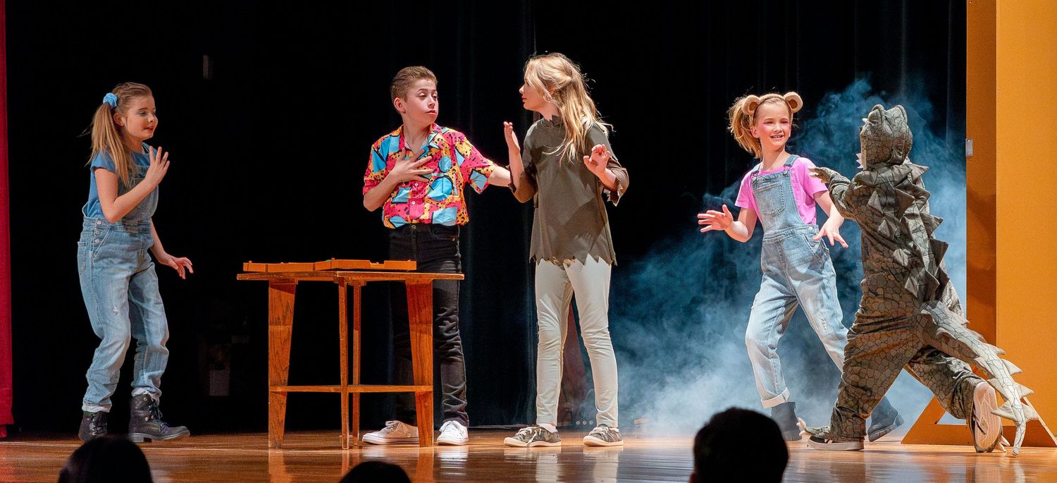 Stage performance featuring actors and a creature costume amid theatrical smoke effects.
