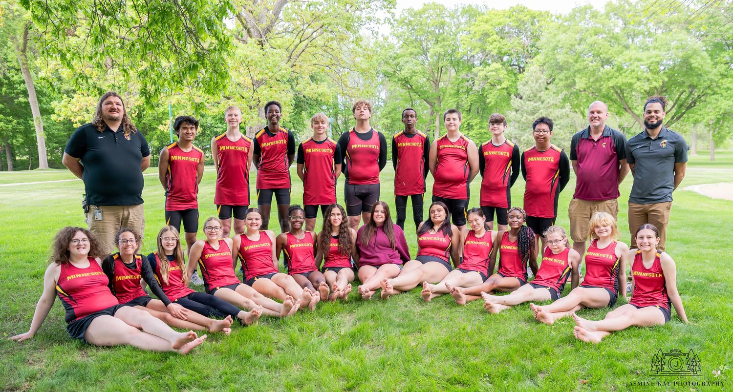 A group wearing red shirts sits together outdoors on grass during a sunny summer day.