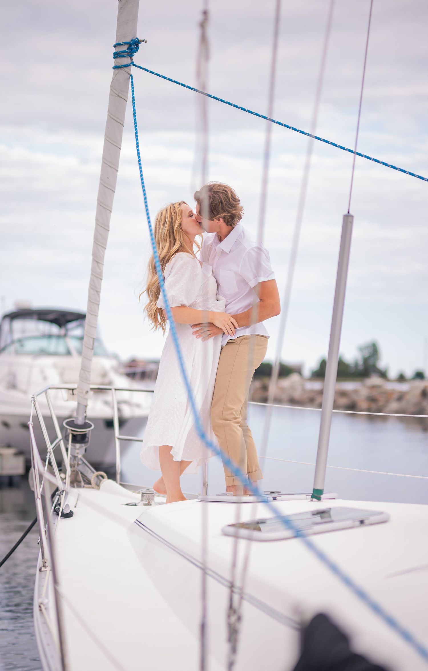 A romantic couple embraces on the deck of a sailboat during a cloudy day at the marina.