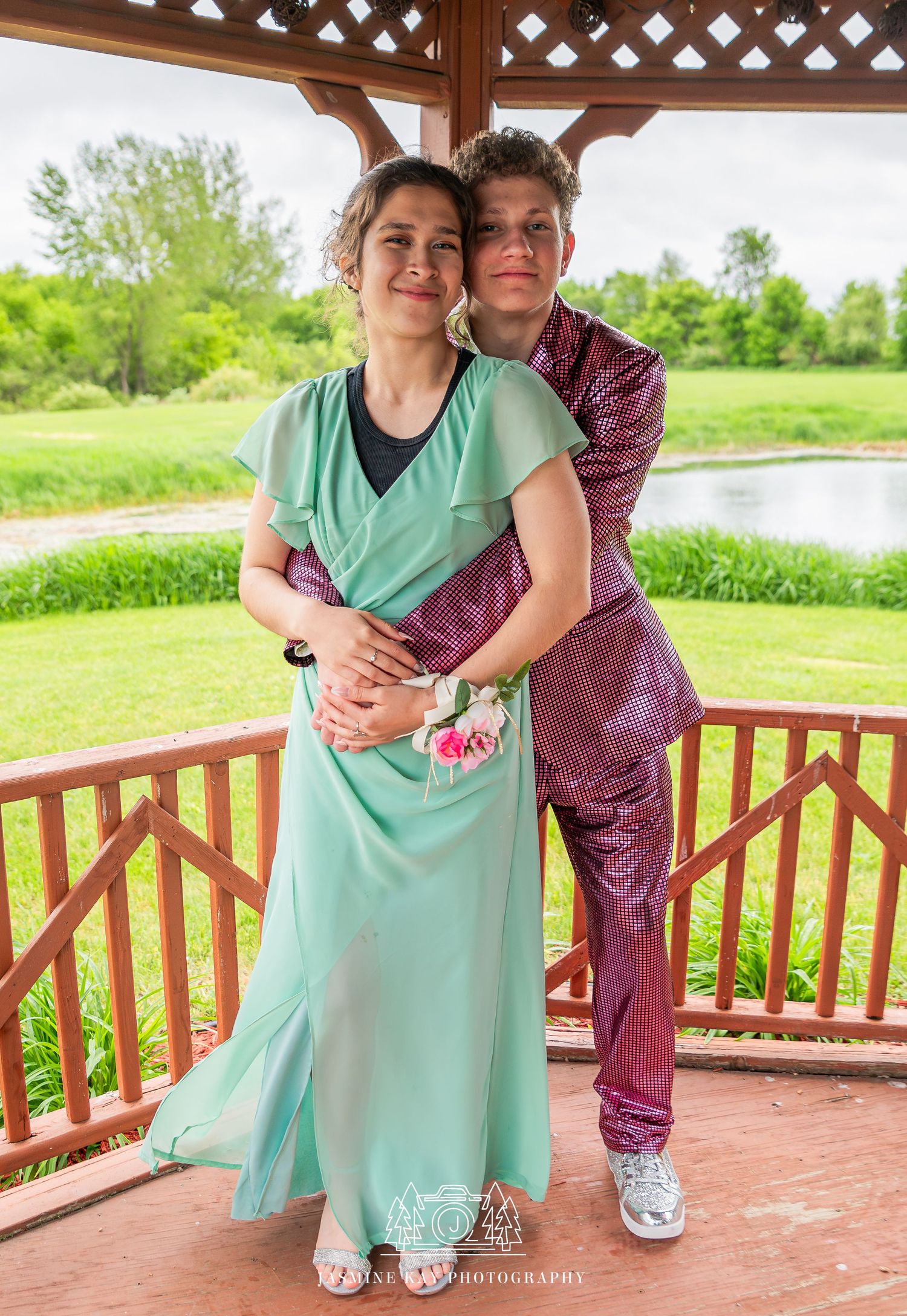 A couple in mint green and burgundy outfits share tender moments on a wooden deck gazebo with lattice details.