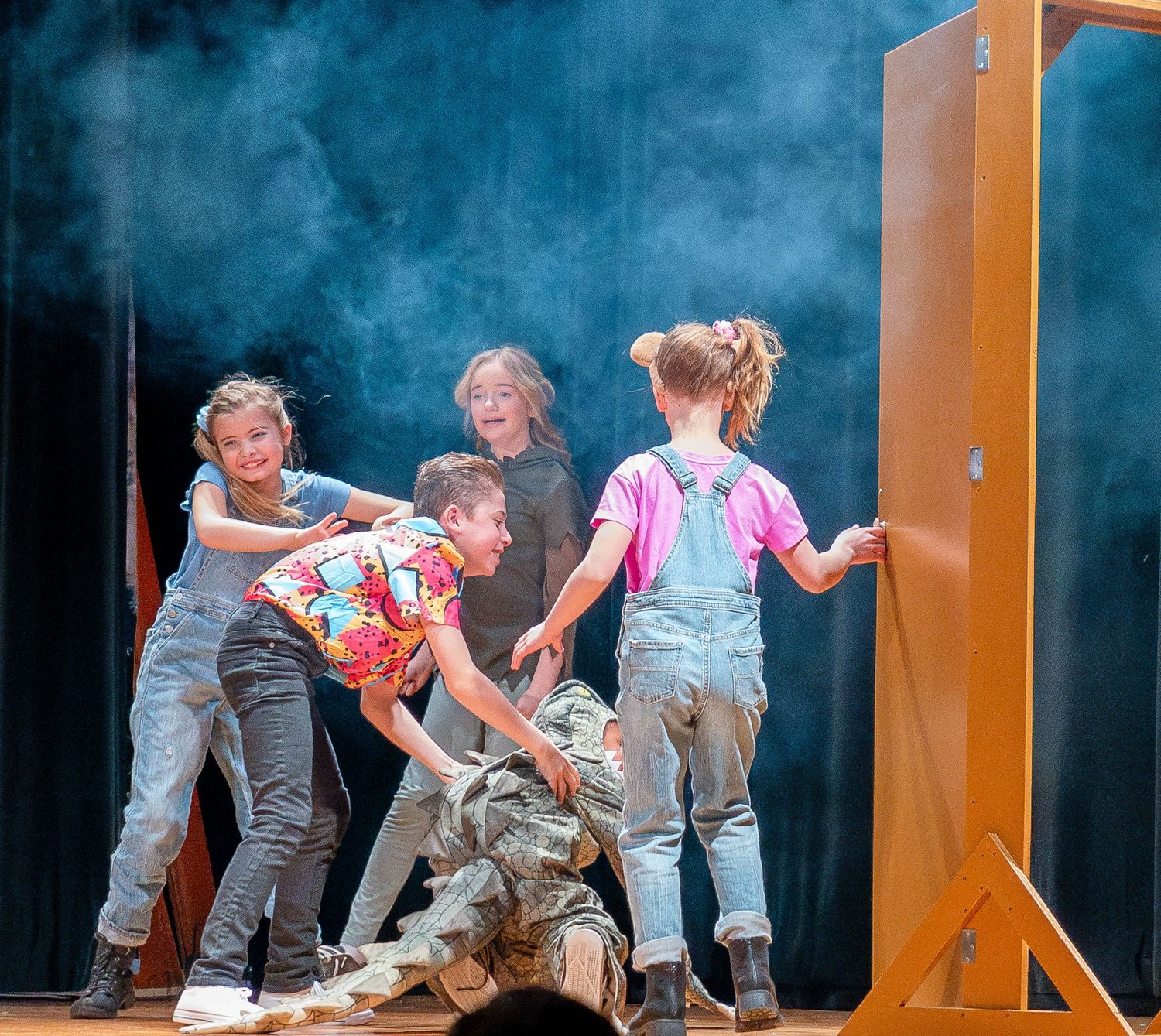 Performers act out an energetic scene on stage with dramatic lighting and smoke effects during a theatrical production.
