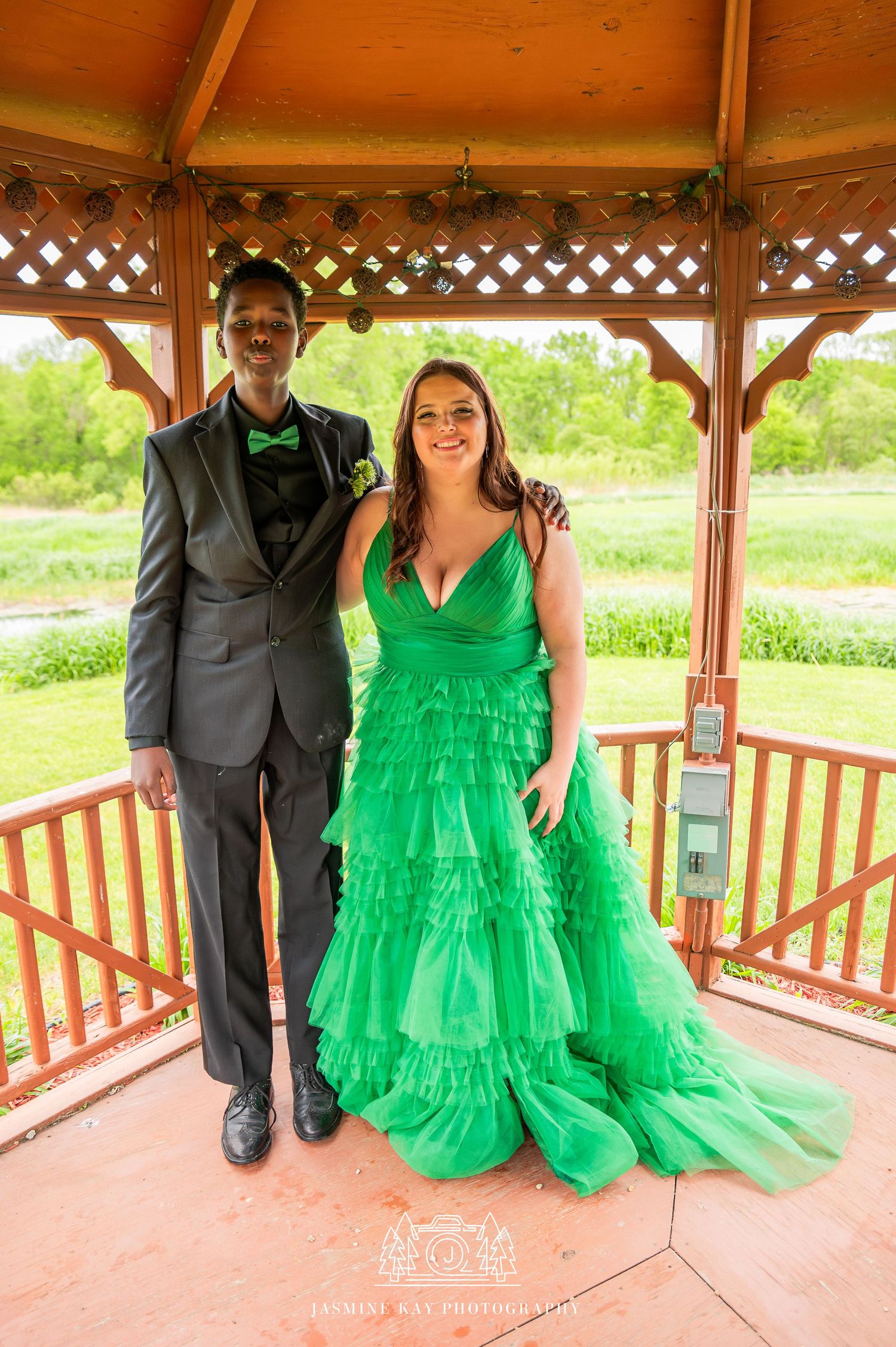 A couple poses in a gazebo, with one wearing a black suit and the other in a vibrant green tulle dress.