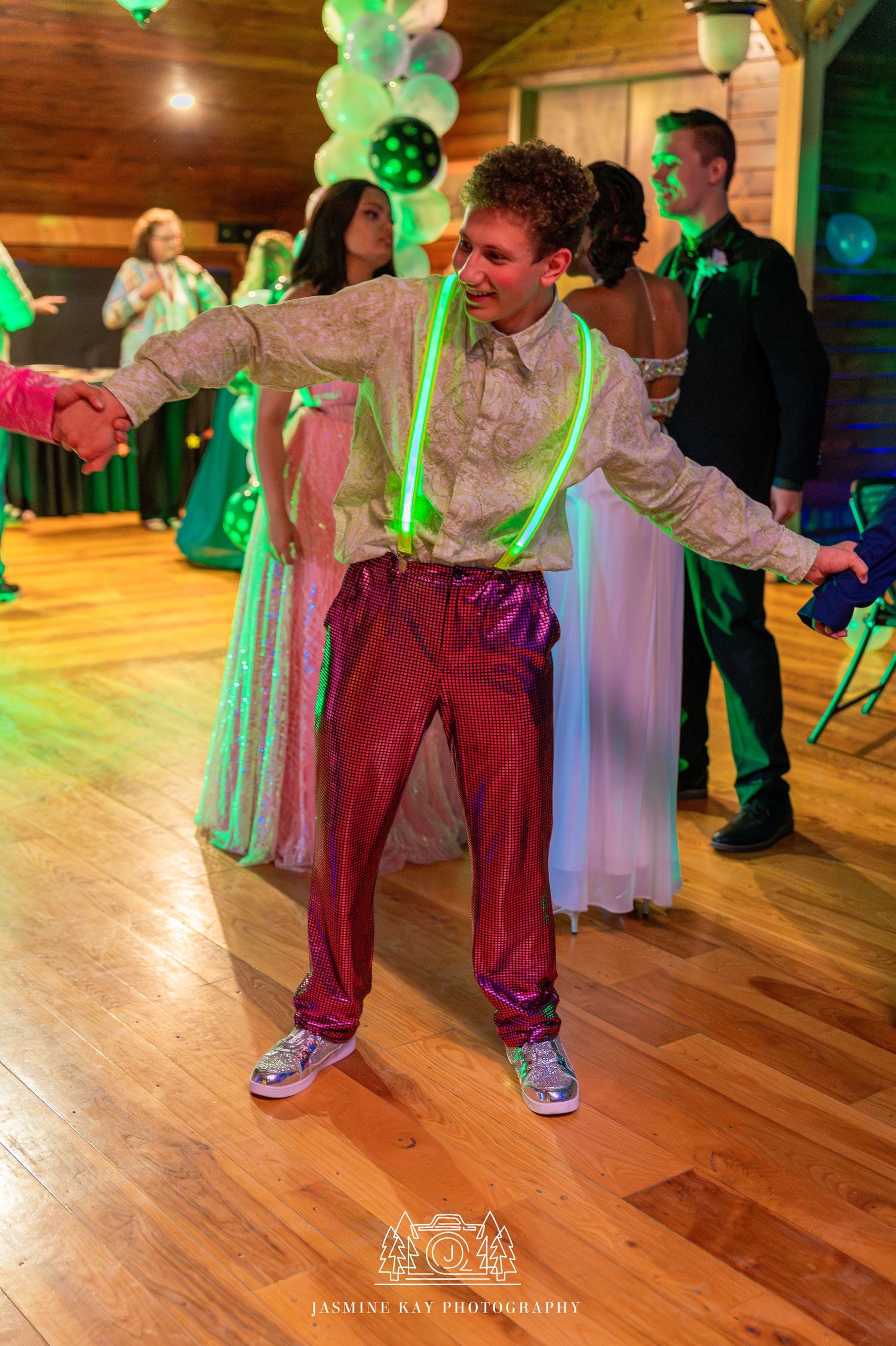 People dancing at a wedding reception with green lighting and wooden floors in a rustic venue.