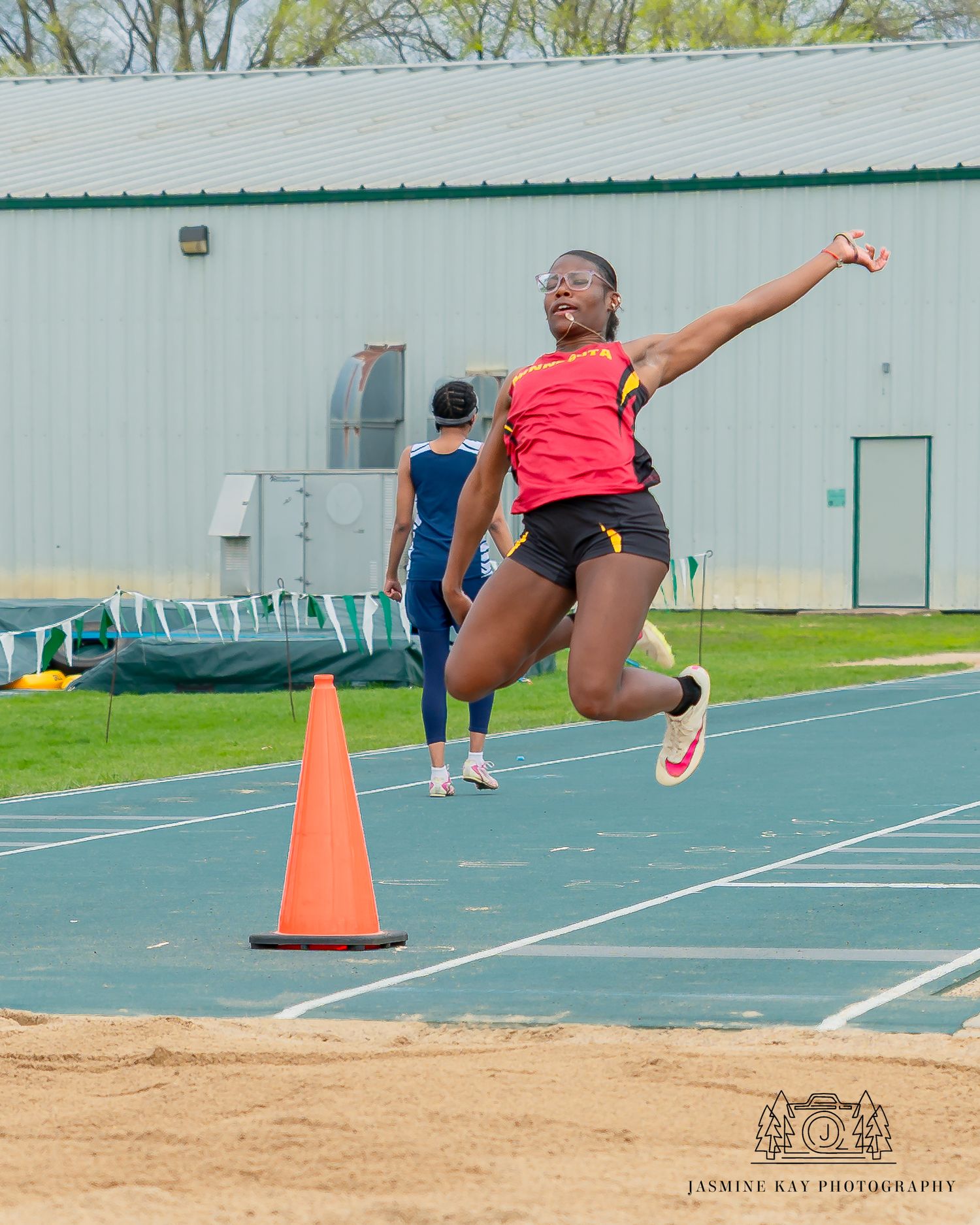 Sequence of long jump athlete performing horizontal jump into sand pit at outdoor track facility.