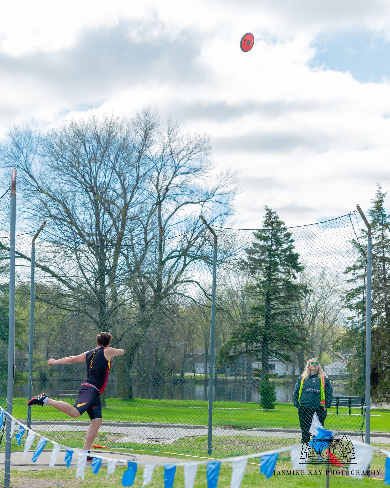 A person playing frisbee in a park performs a leaping catch against a cloudy sky with bare trees in background.