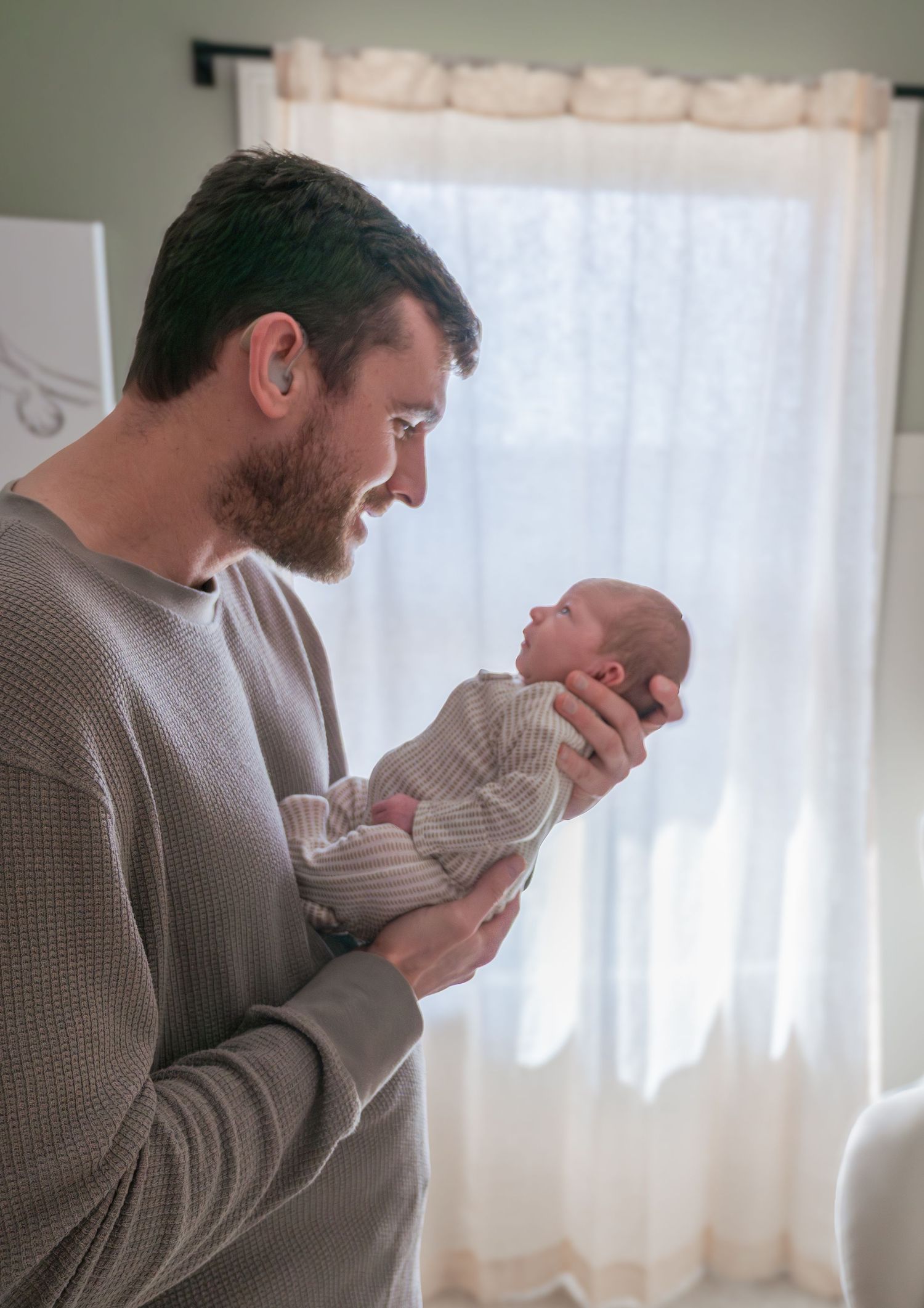 Parent holding and gazing lovingly at newborn baby near window in gentle morning light.