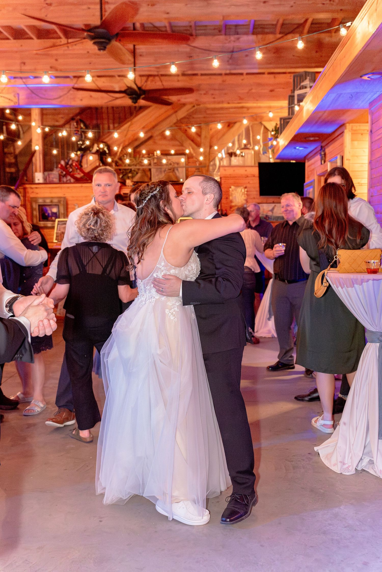 Couples dance under string lights at rustic barn wedding reception.