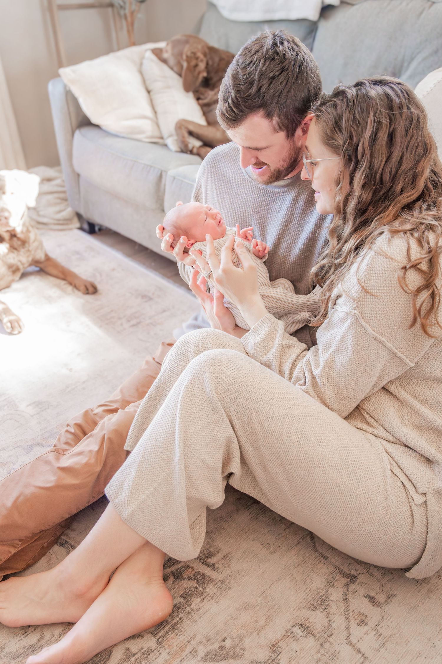 A family lies together on a light colored carpet while bonding with their newborn baby in a cozy home setting.