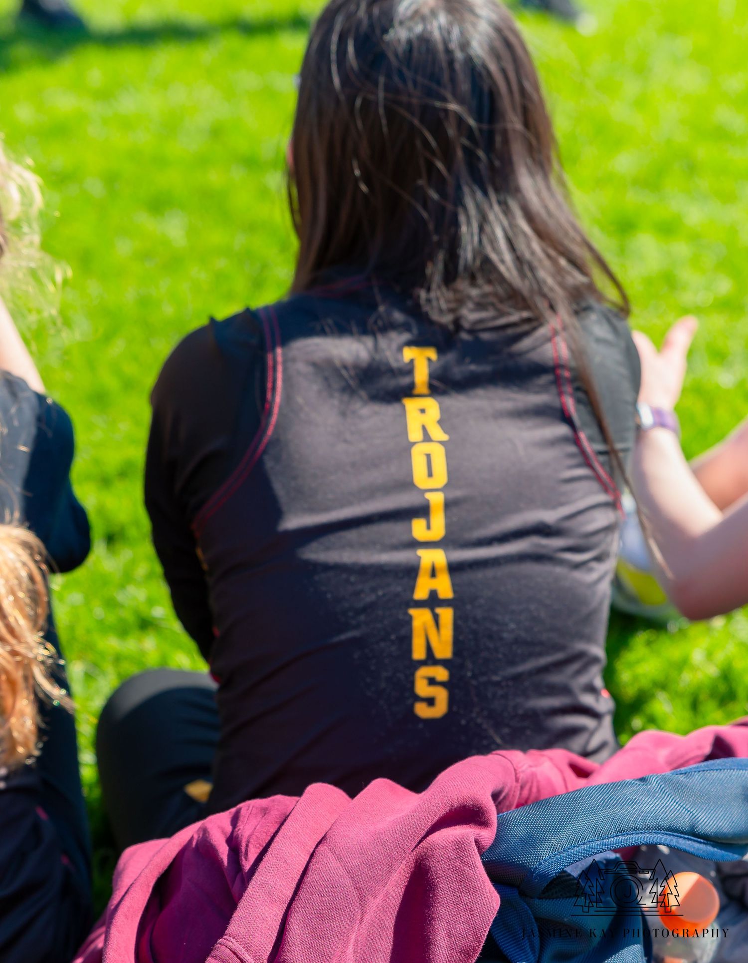 Row of black t-shirts with numbers worn by team members sitting on grass field.