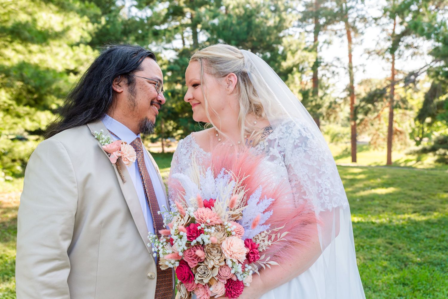 Romantic outdoor wedding portrait with bright pink floral bouquet against green foliage.