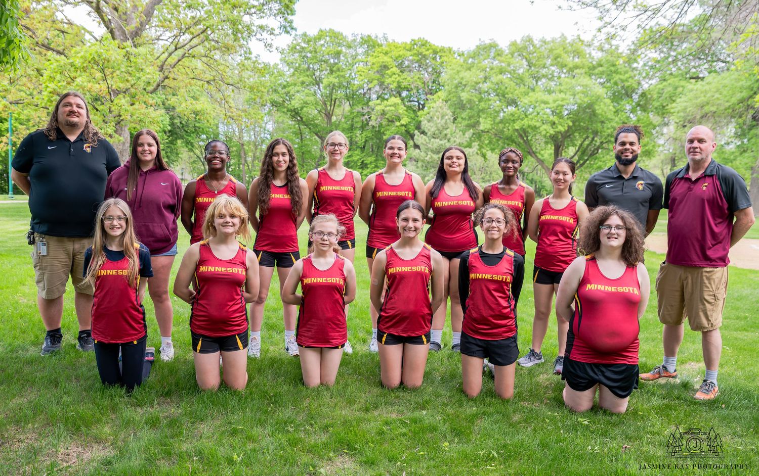 A group in red shirts sits together on grassy hill for an outdoor photo session in springtime.