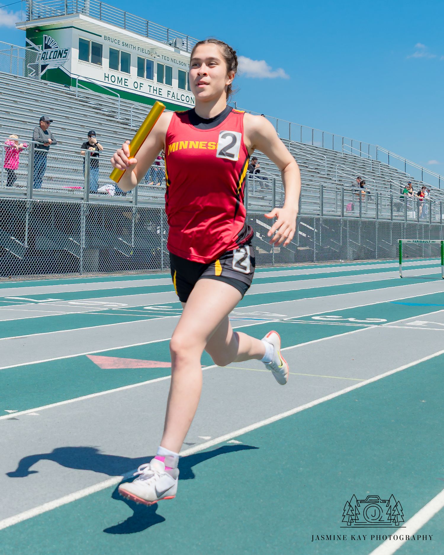 Track athlete in red uniform runs with baton during relay race on outdoor track.