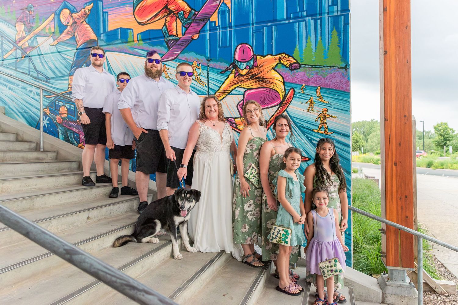 A group of people in colorful attire stand together on outdoor steps with vibrant murals in the background.