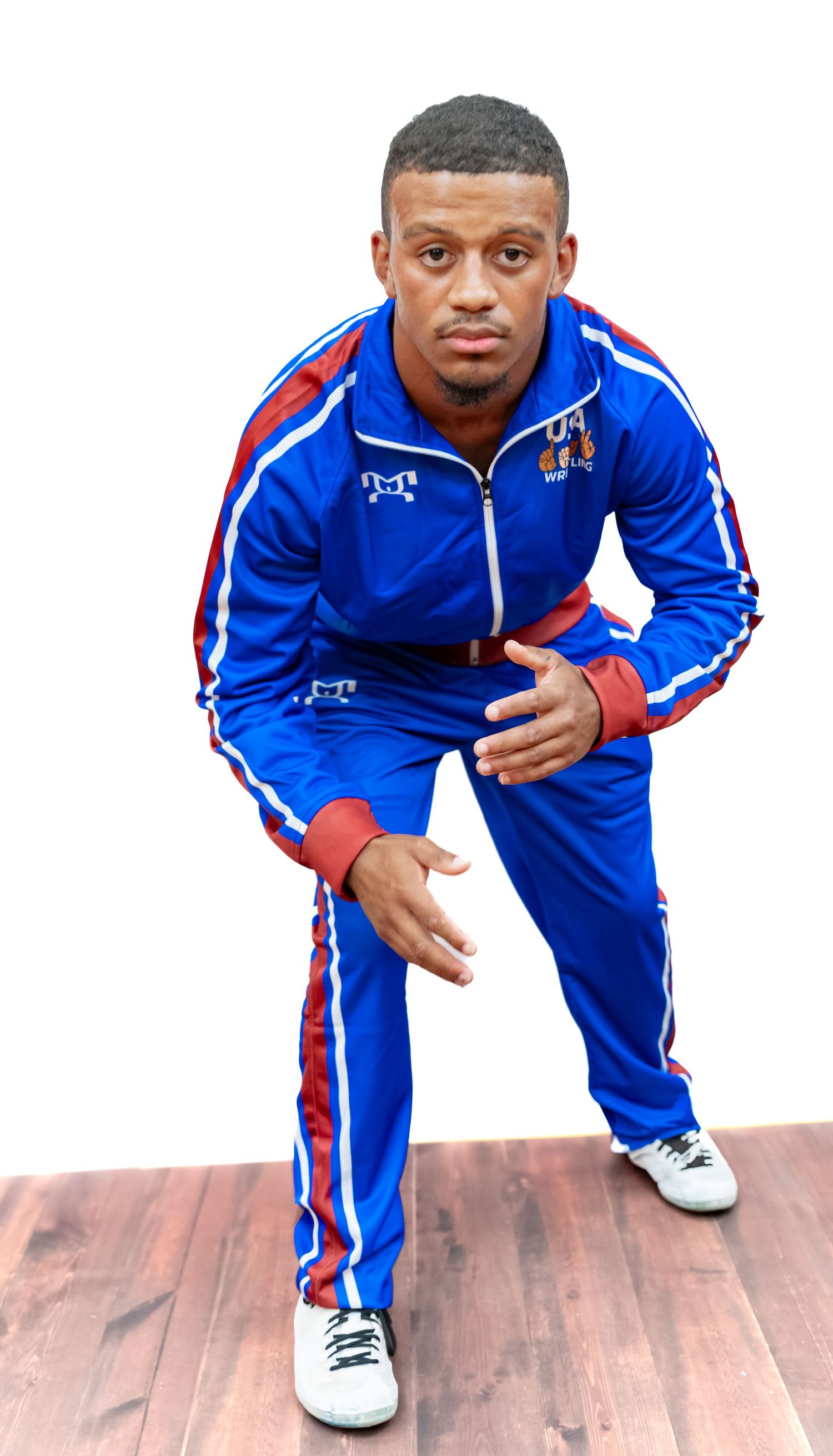 Athlete in blue USA Wrestling uniform shows various crouching stances on hardwood floor.