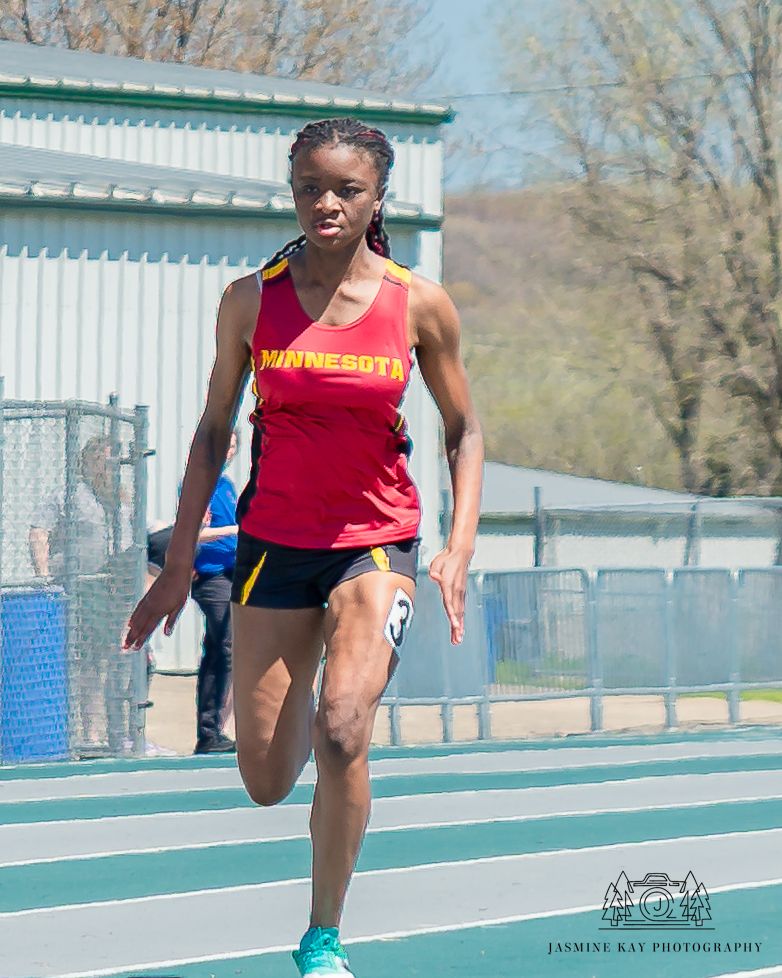 Track athlete demonstrates explosive power during sprint training on blue running track in outdoor stadium.
