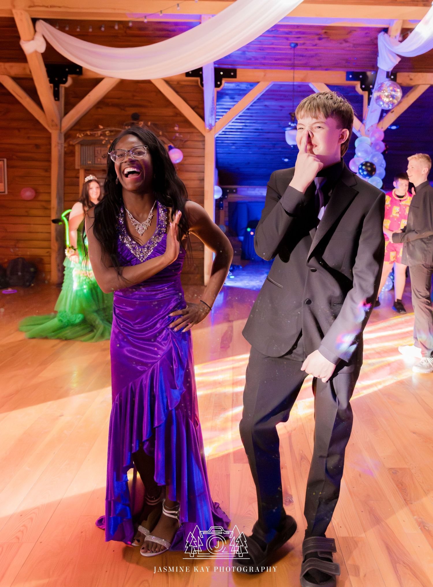 Couple dancing and laughing together at a wedding reception in a rustic wooden venue with purple lighting.
