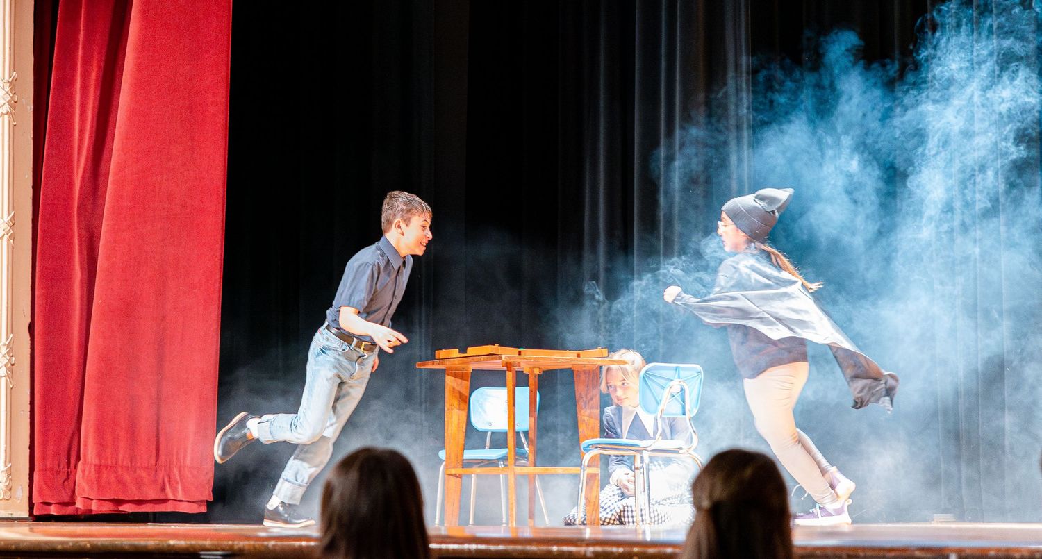 Theater stage with dramatic blue lighting and smoke effects between red curtain pillars.