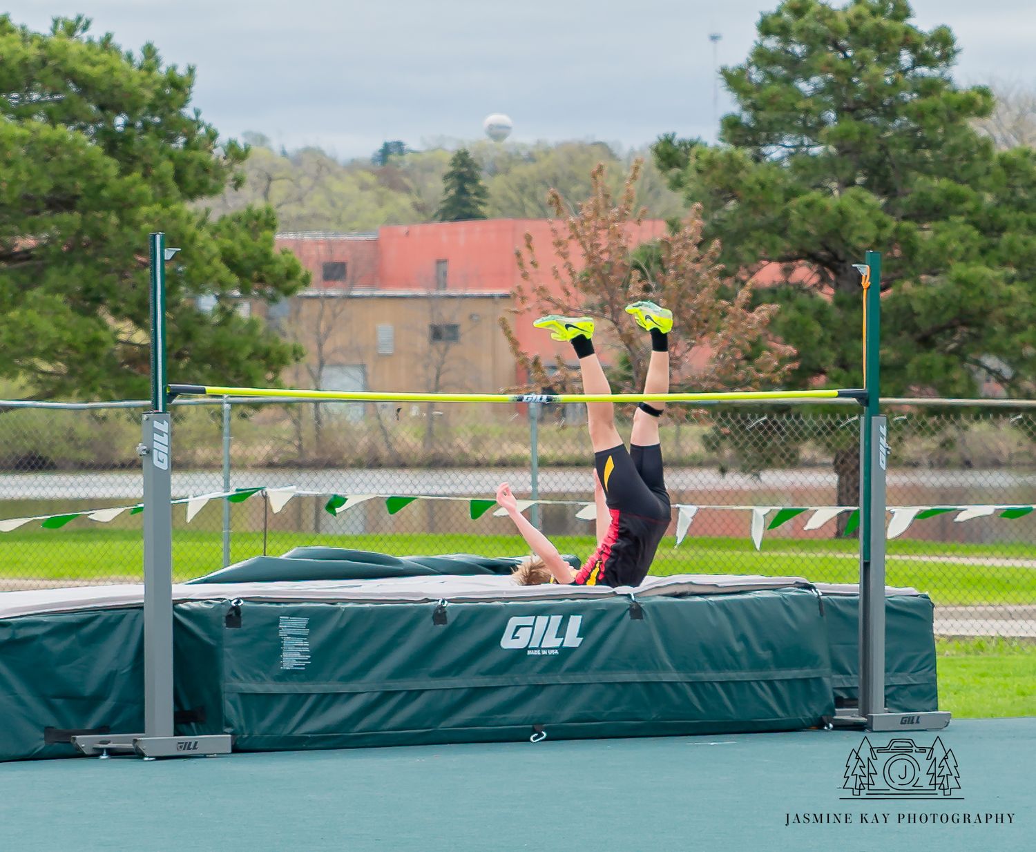Athlete performing high jump technique over bar at track and field facility with landing mat.