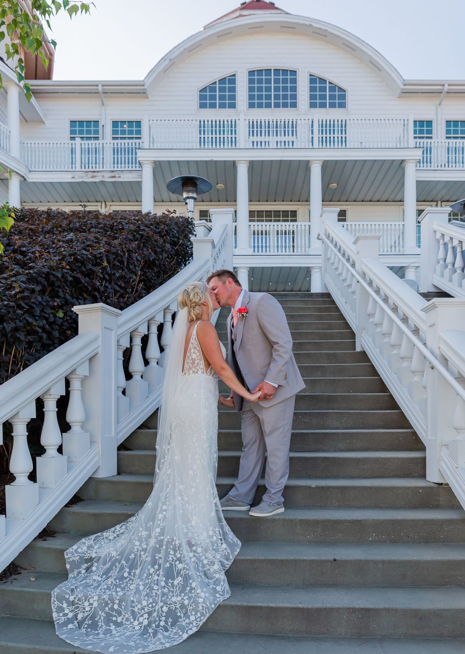 Newlyweds sharing intimate moment on grand white staircase of elegant venue.