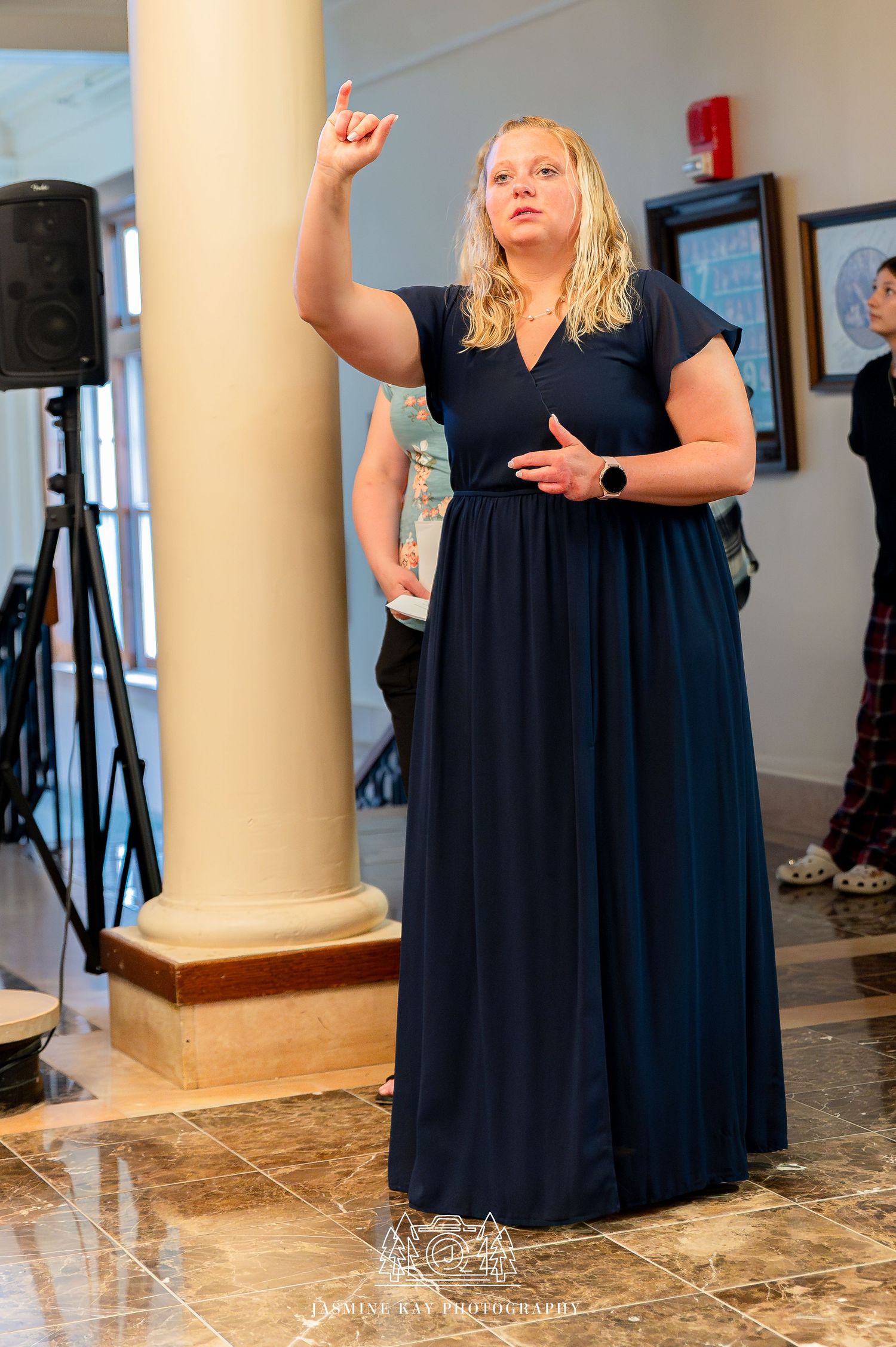 A person in a flowing black dress poses expressively in a room with marble floors and columns.