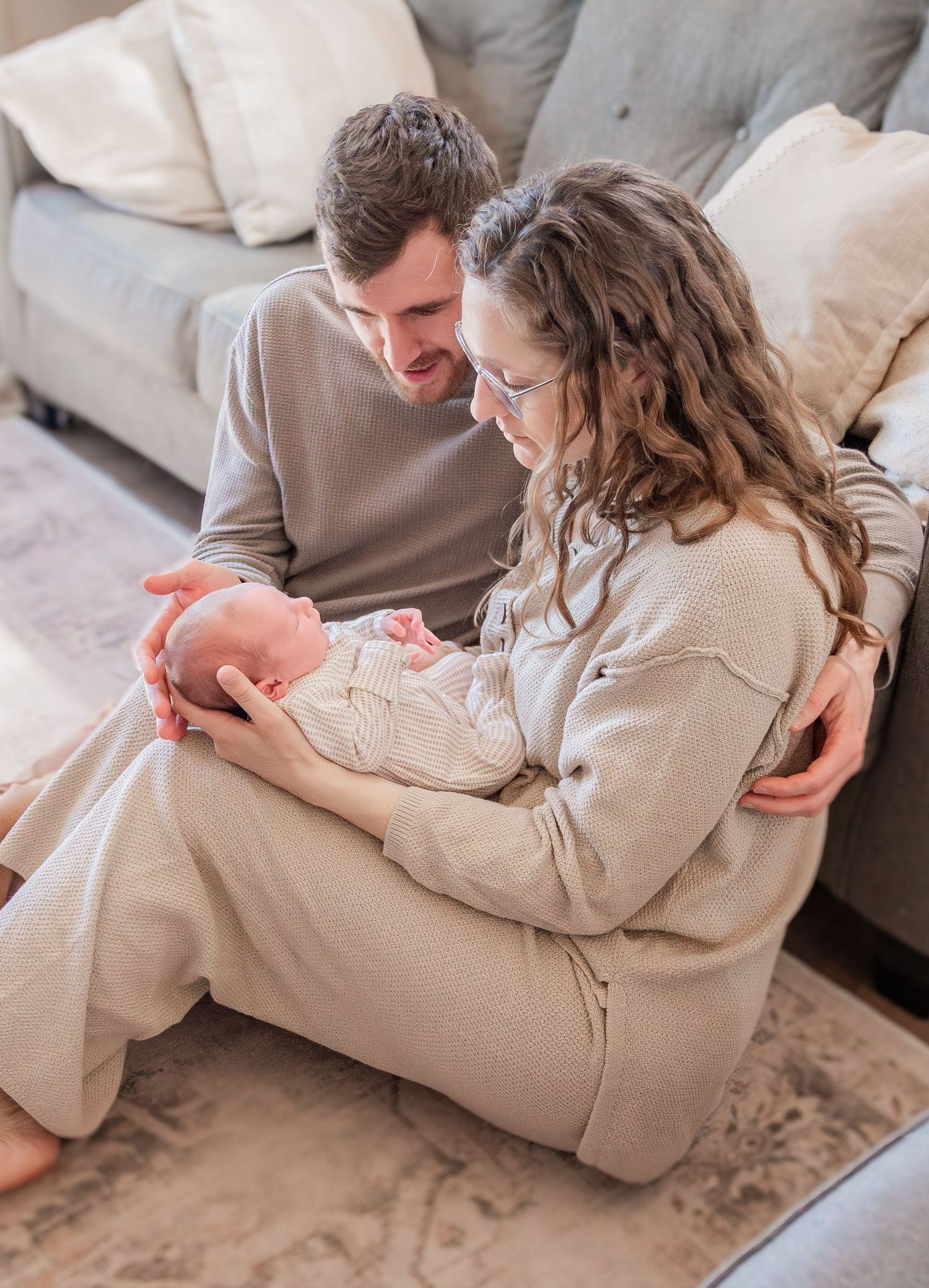A couple in beige outfits sits casually together on a concrete floor in a modern minimalist setting.