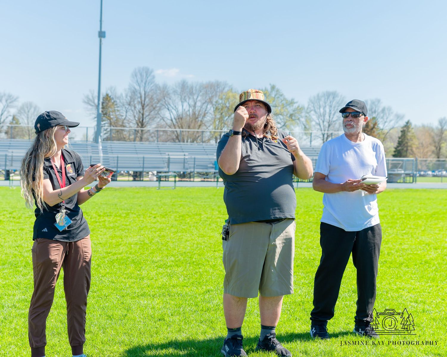 Track and field athletes gathered on sunny grass field for discus throwing practice.
