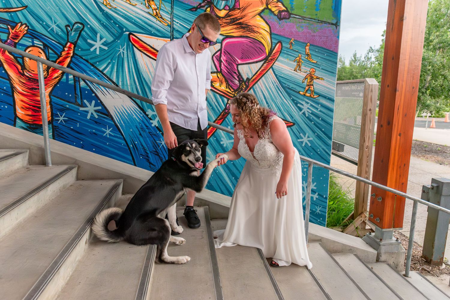 A black cat sits near colorful street art murals while people walk past on a covered walkway.